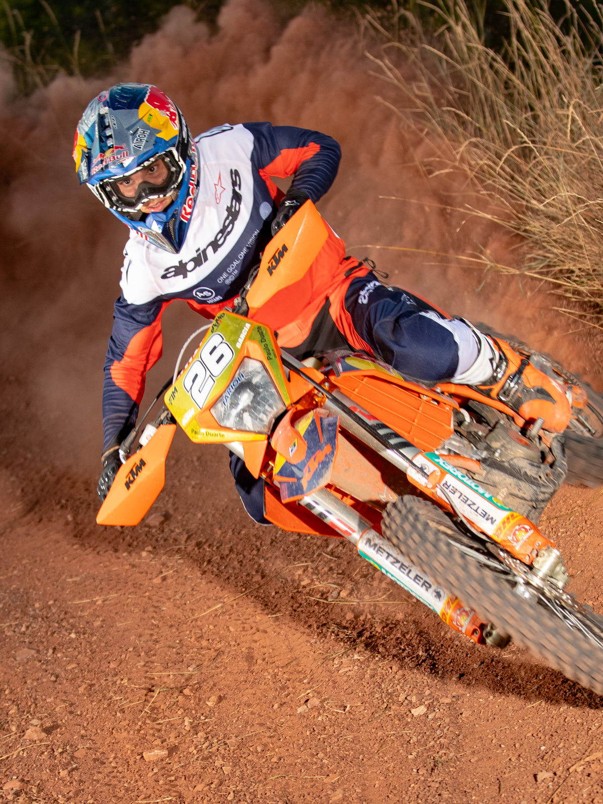Enduro rider in action on an orange dirt bike, wearing the Alpinestars Pro-Dura Jersey in Navy, Hot Orange, and White, featuring a lightweight and breathable design with bold branding for off-road performance.