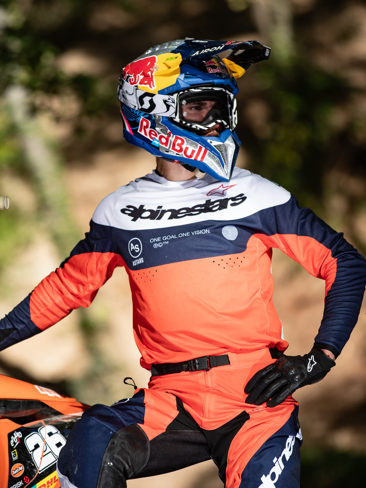 Motocross rider wearing the Alpinestars Pro-Dura Jersey in Navy, Hot Orange, and White, featuring bold chest branding and laser perforations, paired with a Red Bull racing helmet, professional gear for enduro and off-road performance.