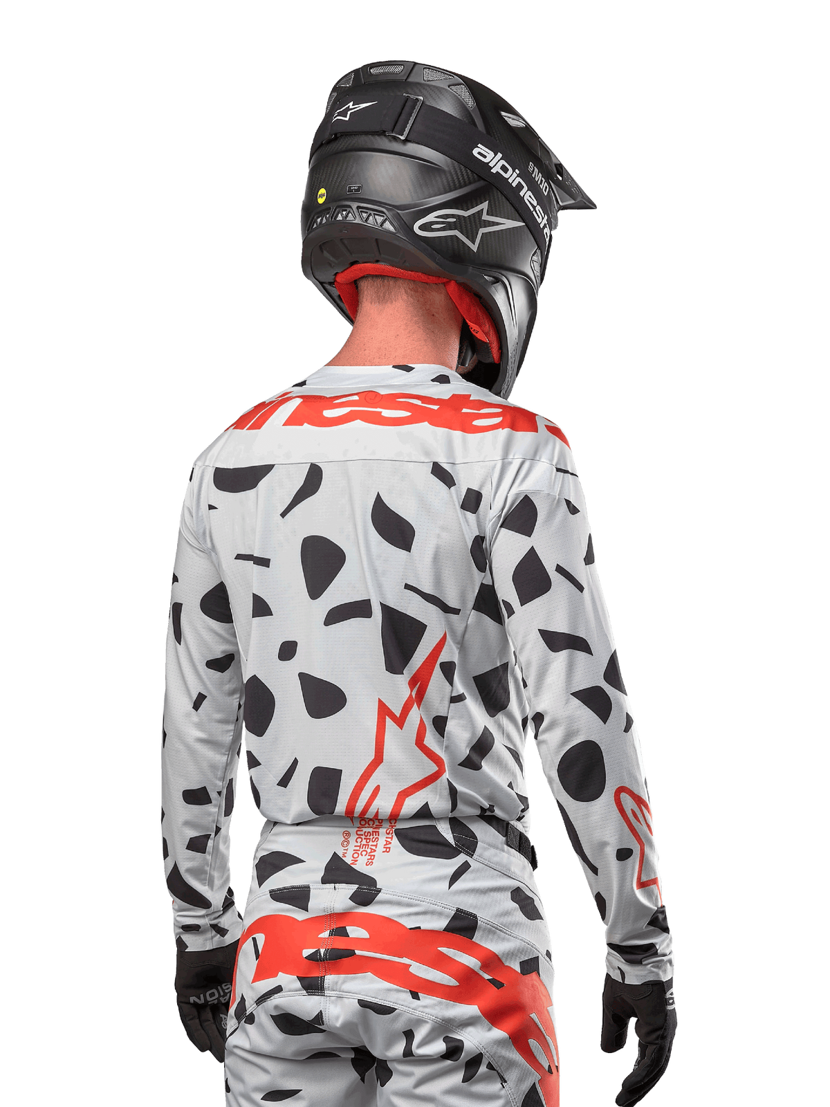 Motocross rider from the back wearing the Alpinestars 2024 Techstar Rantera Jersey in Haze Gray Camo, featuring a light gray base with black graphic spots and bold red Alpinestars logos on the back and shoulders, paired with matching pants and a black helmet.
