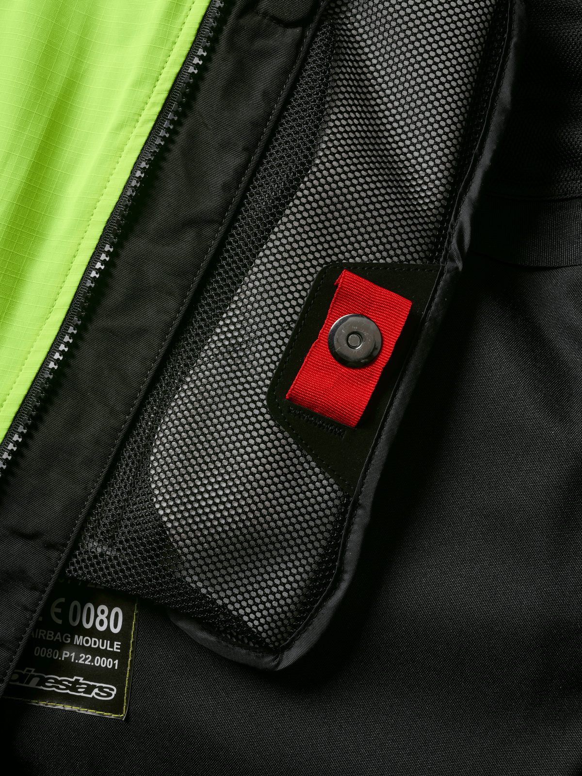 Alpinestars Tech-Air® 3 V2 System detail, close-up of internal mesh pocket with red pull tab and snap fastener, vibrant yellow fluo panel, black textile construction showing airbag module label and zipper