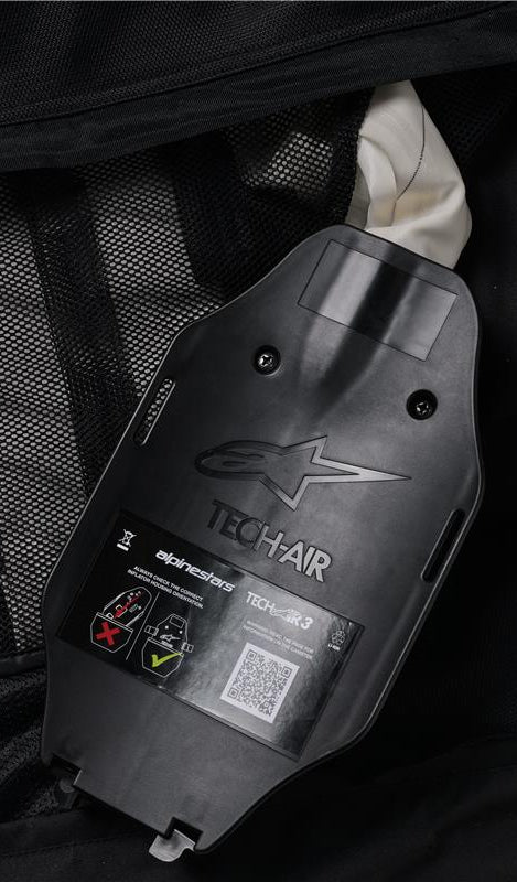 Alpinestars Tech-Air 3 V2 System, Internal view of the gas inflator and ECU housing, black plastic with embossed logo, safety label with QR code and installation diagrams, black mesh interior lining, detail of the user-serviceable autonomous airbag system