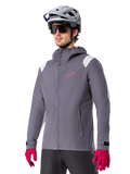 Alpinestars A-Dura Rain Jacket, Mountain Bike Rain Jacket, Dark Titanium Gray with pink logo and white shoulder accents, hooded design with front pockets, worn with pink gloves and a light gray cycling helmet