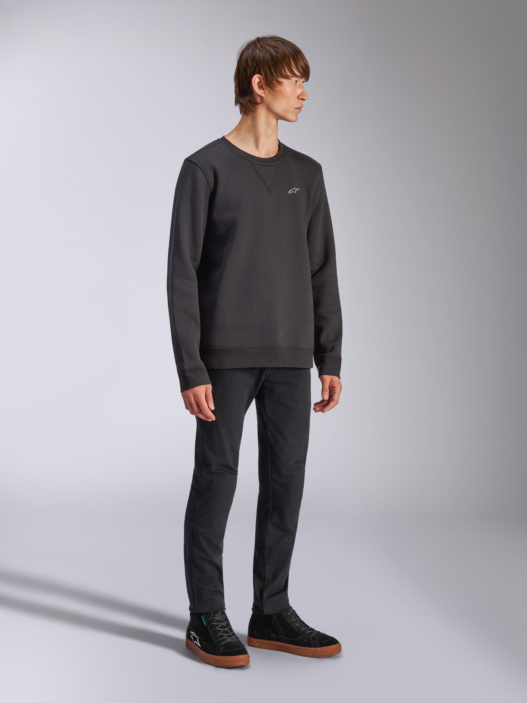 Alpinestars Positive Crew, Pullover Sweatshirt, Black, small white Alpinestars logo on the chest, ribbed collar with V-stitch detail, ribbed cuffs and hem, worn by a model with black trousers and sneakers, casual motorsport-inspired streetwear