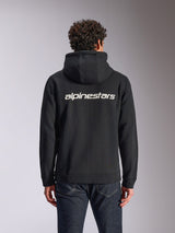 Alpinestars Transverse Hoodie, casual streetwear, black with white Alpinestars word logo on the back, zip-front hooded fleece, long sleeves, worn by a model with dark denim jeans, modern motorsport-inspired design