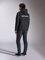 Alpinestars Transverse Hoodie, Black zip-front fleece, back view featuring a white Alpinestars word logo across the shoulders, worn with dark blue jeans and black sneakers, casual motorsport-inspired streetwear
