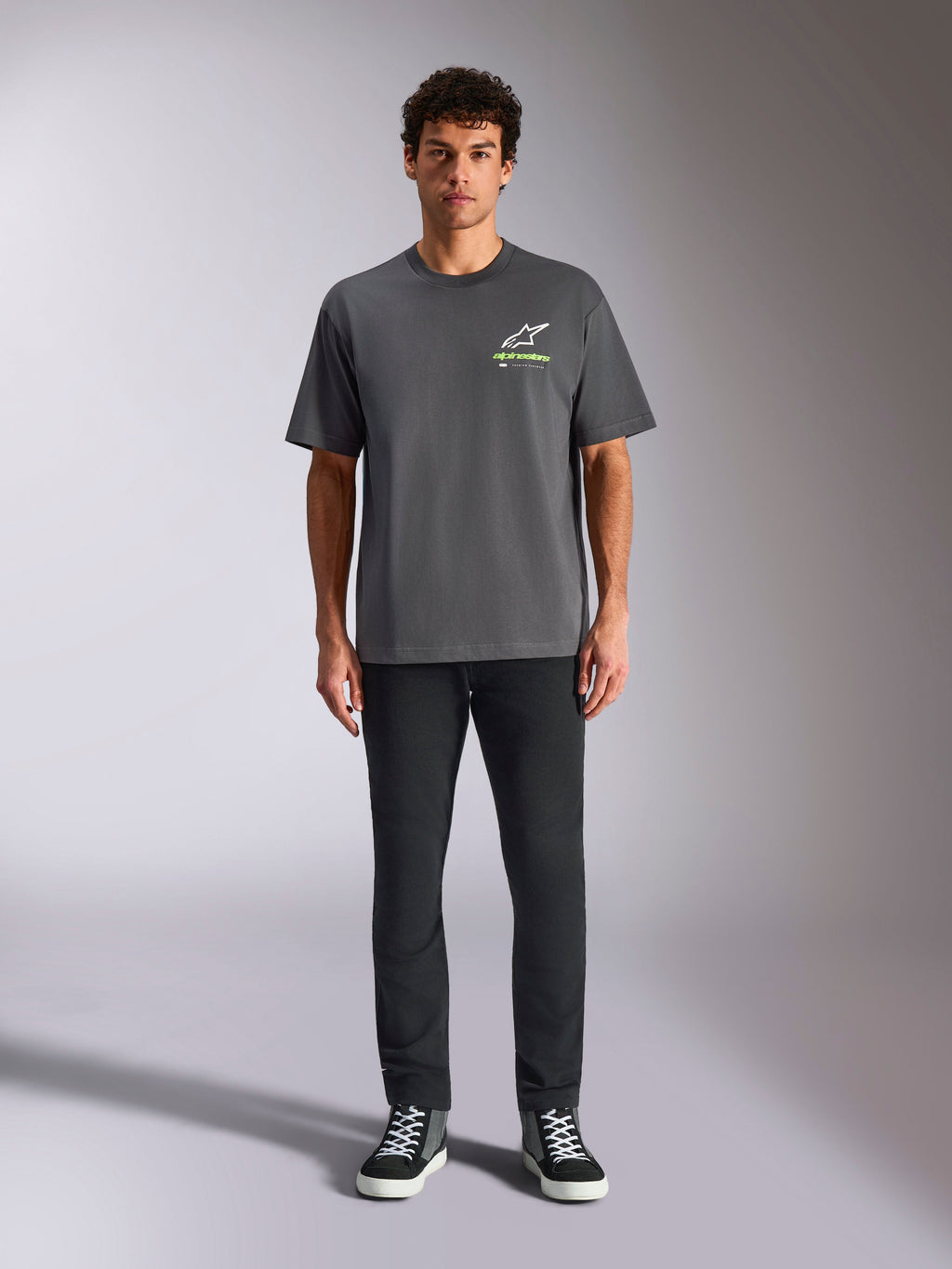 Alpinestars Overhang Oversized CSF Tee, Short Sleeve T-Shirt, Charcoal Gray, featuring a front white and lime green Alpinestars logo, worn by a model with black pants and sneakers, relaxed casual streetwear