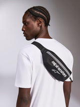 Alpinestars Only Linear Hip Bag, Black and White, worn crossbody over a white t-shirt, featuring white Alpinestars logo branding and vertical zipper closure, compact streetwear accessory.