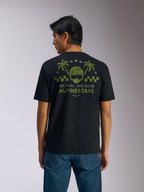 Alpinestars Order CSF Tee, Short Sleeve T-Shirt, Black, Back View, Olive Green Graphic with Palm Trees and Helmet Logo, 'ONE GOAL. ONE VISION. ALPINESTARS' text, paired with blue jeans, casual motorsport streetwear