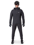 Alpinestars A-Dura Elite Waterproof Jacket, Black, worn with matching cycling pants and gloves, black helmet and sunglasses, featuring a white Astars logo on the chest, high-performance technical design for mountain biking