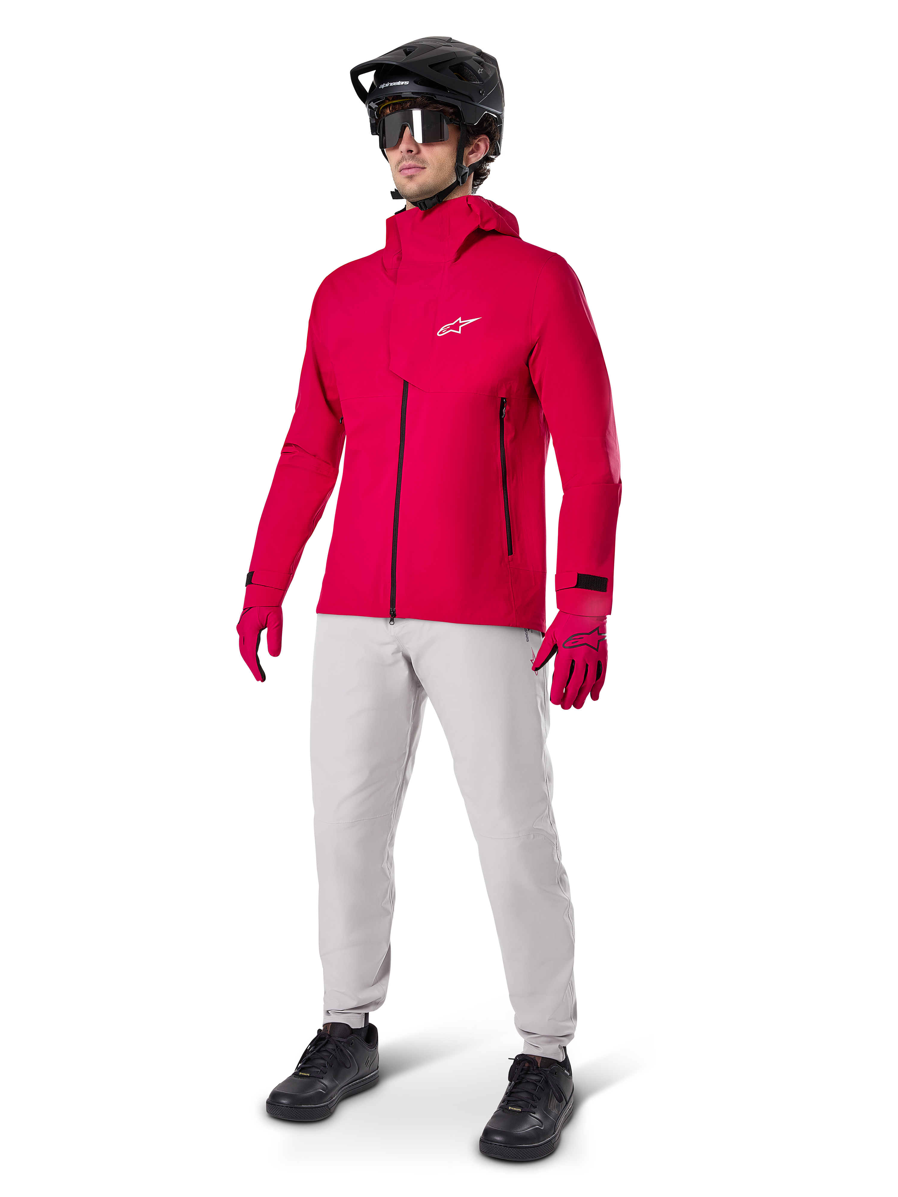 Male cyclist wearing the Alpinestars A-Dura Elite Waterproof Jacket in Red Fluo, paired with light grey technical pants, red gloves, black MTB helmet with goggles, and black shoes, complete high-performance outfit for mountain biking