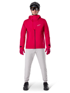 Alpinestars A-Dura Elite Waterproof Jacket, Red Fluo, technical mountain bike jacket worn with a black MTB helmet, sunglasses, matching red gloves, and light grey pants, full-body view of all-weather cycling gear
