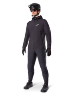 Alpinestars A-Dura Thermal Jacket in Black, worn by a male rider with complete mountain bike gear including a black helmet, sunglasses, and riding pants, lightweight insulated hooded jacket for cold-weather cycling performance.