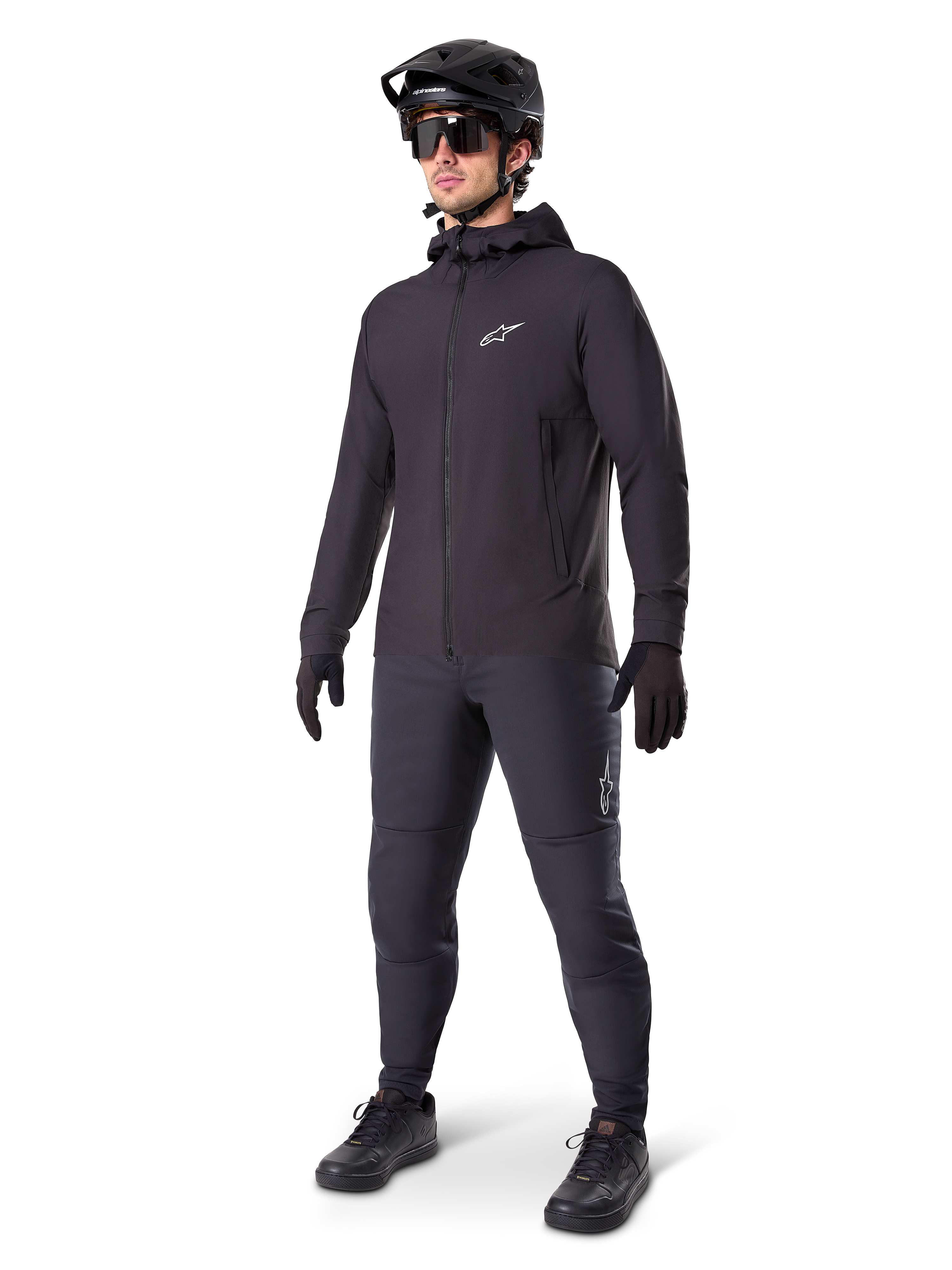 Alpinestars A-Dura Thermal Jacket in Black, worn by a male rider with complete mountain bike gear including a black helmet, sunglasses, and riding pants, lightweight insulated hooded jacket for cold-weather cycling performance.