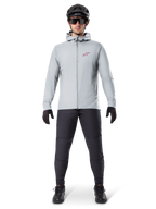 Alpinestars A-Dura Thermal Jacket, Titanium gray, cycling jacket worn with black mountain biking pants, gloves, and helmet, featuring a small red star logo on the chest and a full front zipper, lightweight insulated gear for off-road riding.