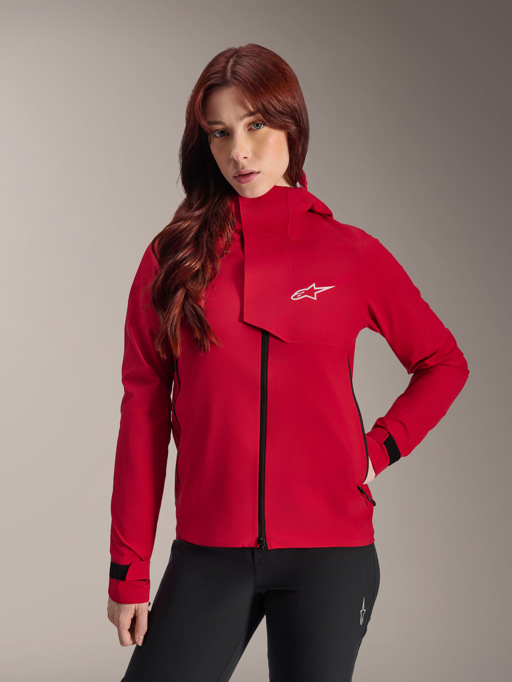 Alpinestars Stella A-Dura Elite Waterproof Jacket, Women's Mountain Bike Jacket, Red Fluo, featuring a front storm flap with a white Alpinestars logo, high collar, and adjustable cuffs, worn with black pants for a technical riding look
