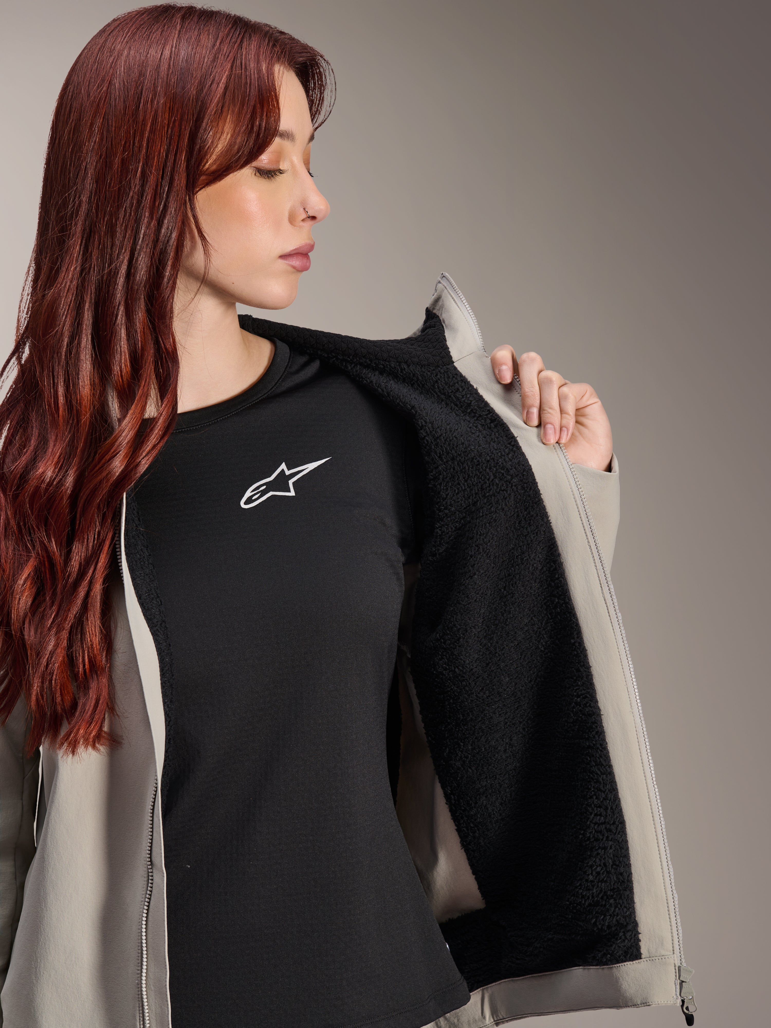 Woman wearing the Alpinestars Stella A-Dura Thermal Jacket in Titanium, showcasing the black textured fleece lining, worn over a black t-shirt with a white star logo, lightweight mountain bike jacket for cold conditions.