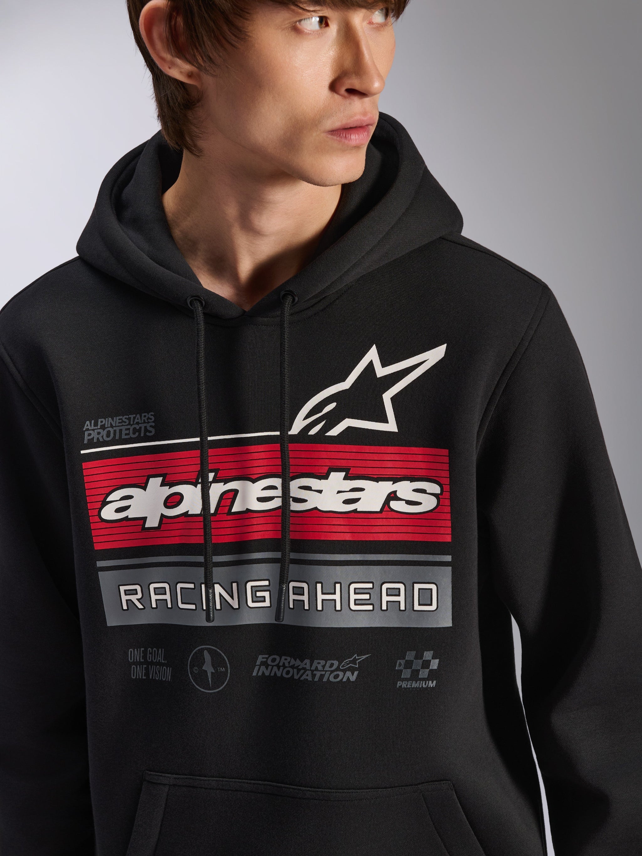 Alpinestars Harken Hoodie, Black pullover fleece hoodie worn by a model, featuring a large graphic on the chest with red and gray stripes, white Alpinestars wordmark and star logo, 'Racing Ahead' text, modern motorsport-inspired casual streetwear.