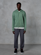 Alpinestars Essentials Ageless Zip Hoodie, Zip-up Hoodie, Cactus Green, worn by a model with dark grey joggers and black sneakers, featuring a small black Alpinestars logo on the chest, relaxed fit, casual streetwear.
