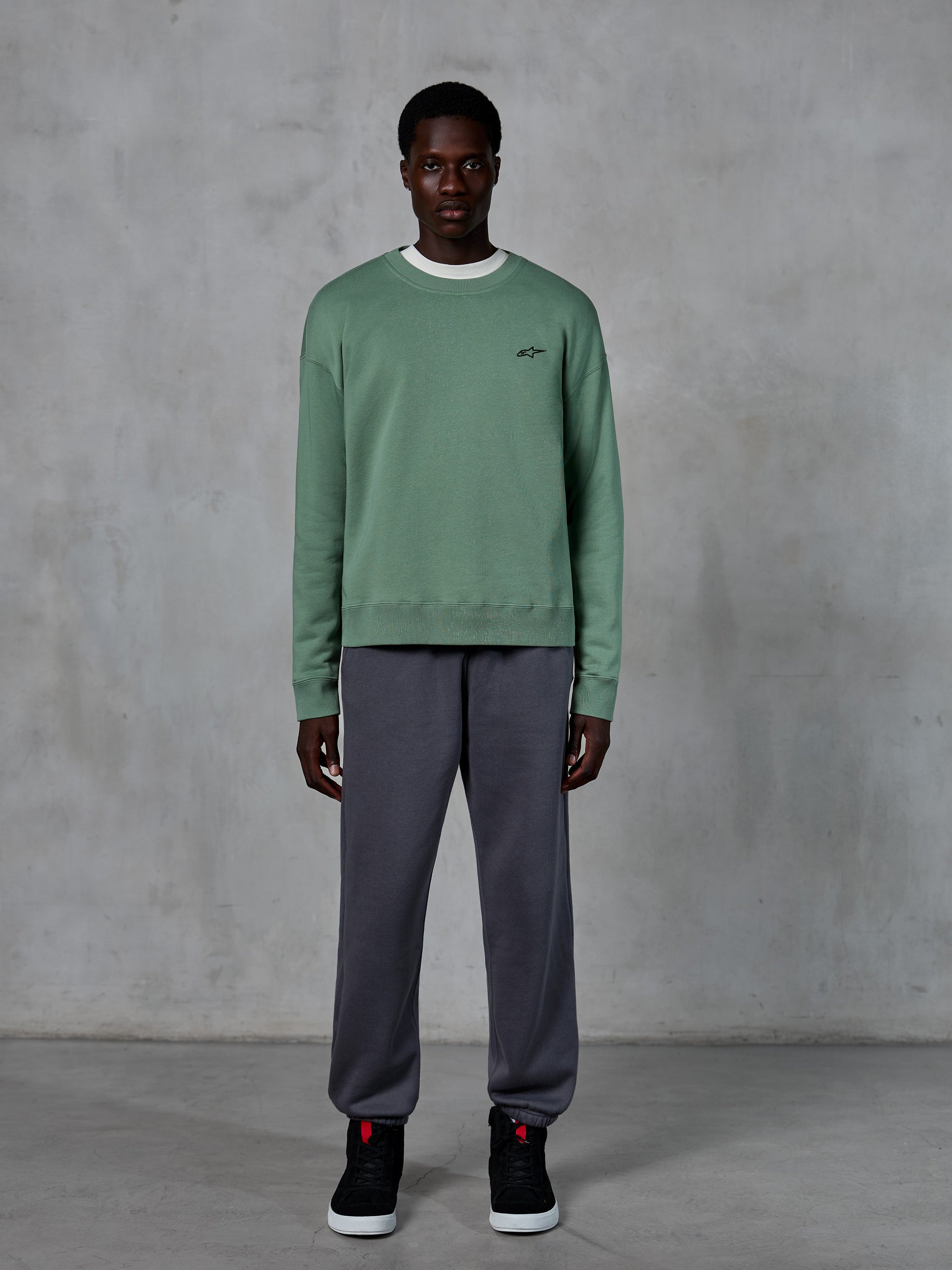 Alpinestars Essentials Ageless Crew, crewneck sweatshirt in Cactus green, featuring a small black chest logo, worn by a model with grey sweatpants and black sneakers, casual motorsport-inspired streetwear