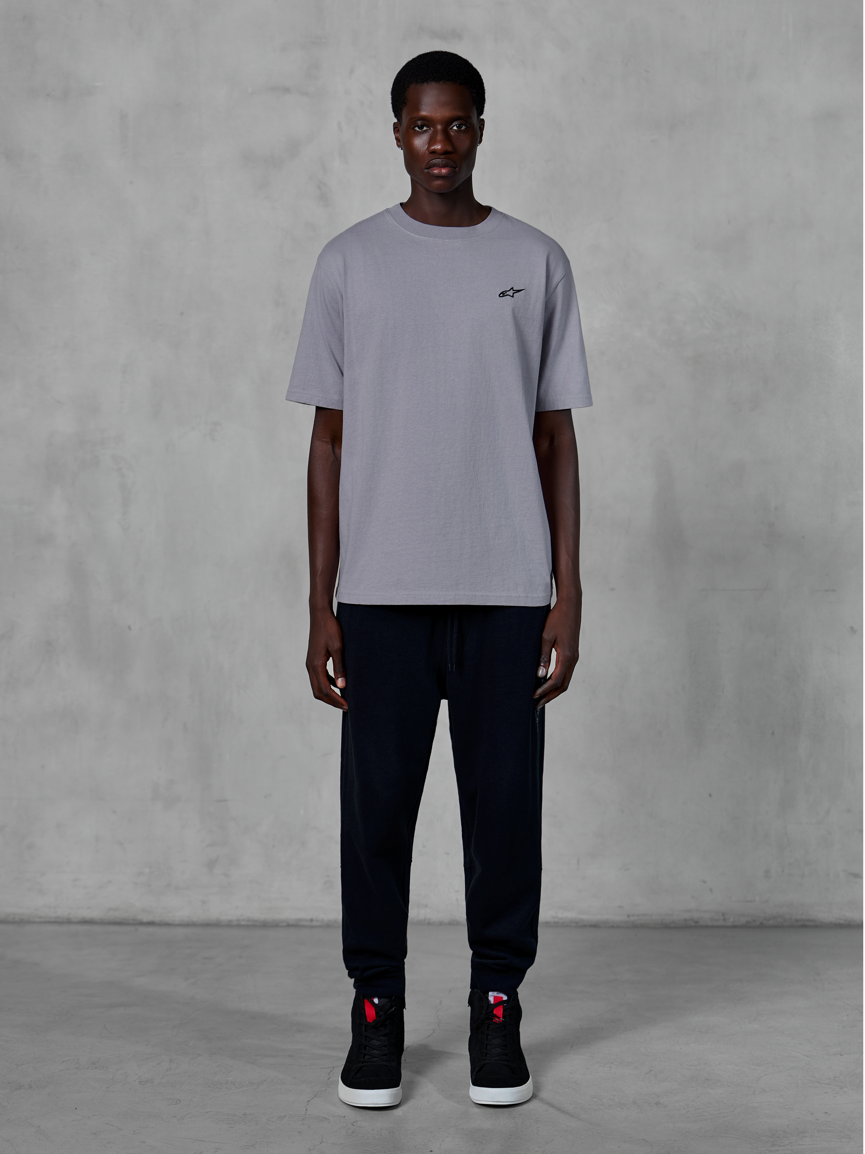 Alpinestars Essentials Ageless SS Tee, Short Sleeve T-Shirt, Silver, featuring a small black logo on the chest, styled with black joggers and sneakers, casual motorsport streetwear