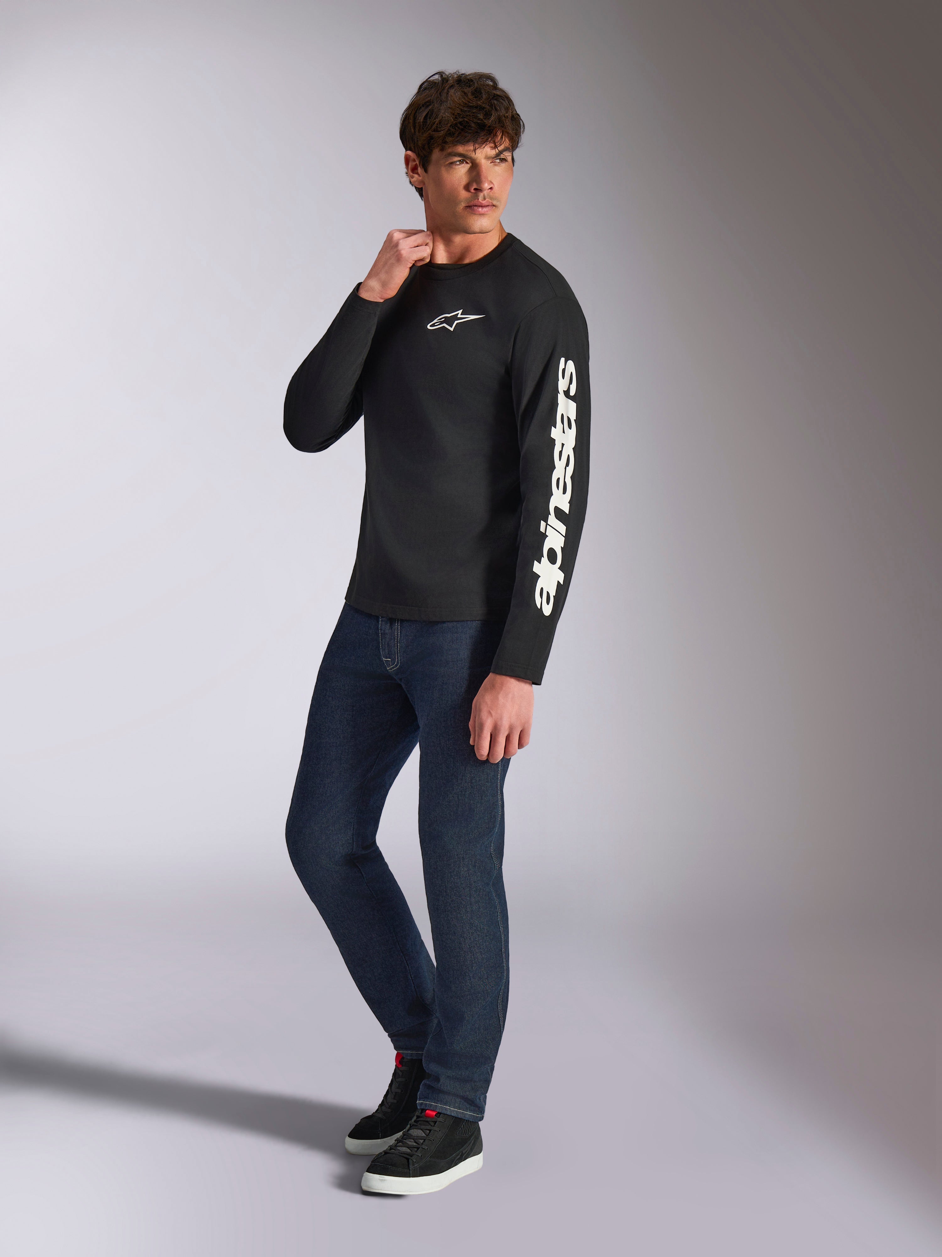 Alpinestars Trackside CSF Tee, Long Sleeve T-Shirt, Black, white vertical Alpinestars branding on sleeve and chest logo, worn by male model with dark blue jeans and sneakers, casual motorsport streetwear