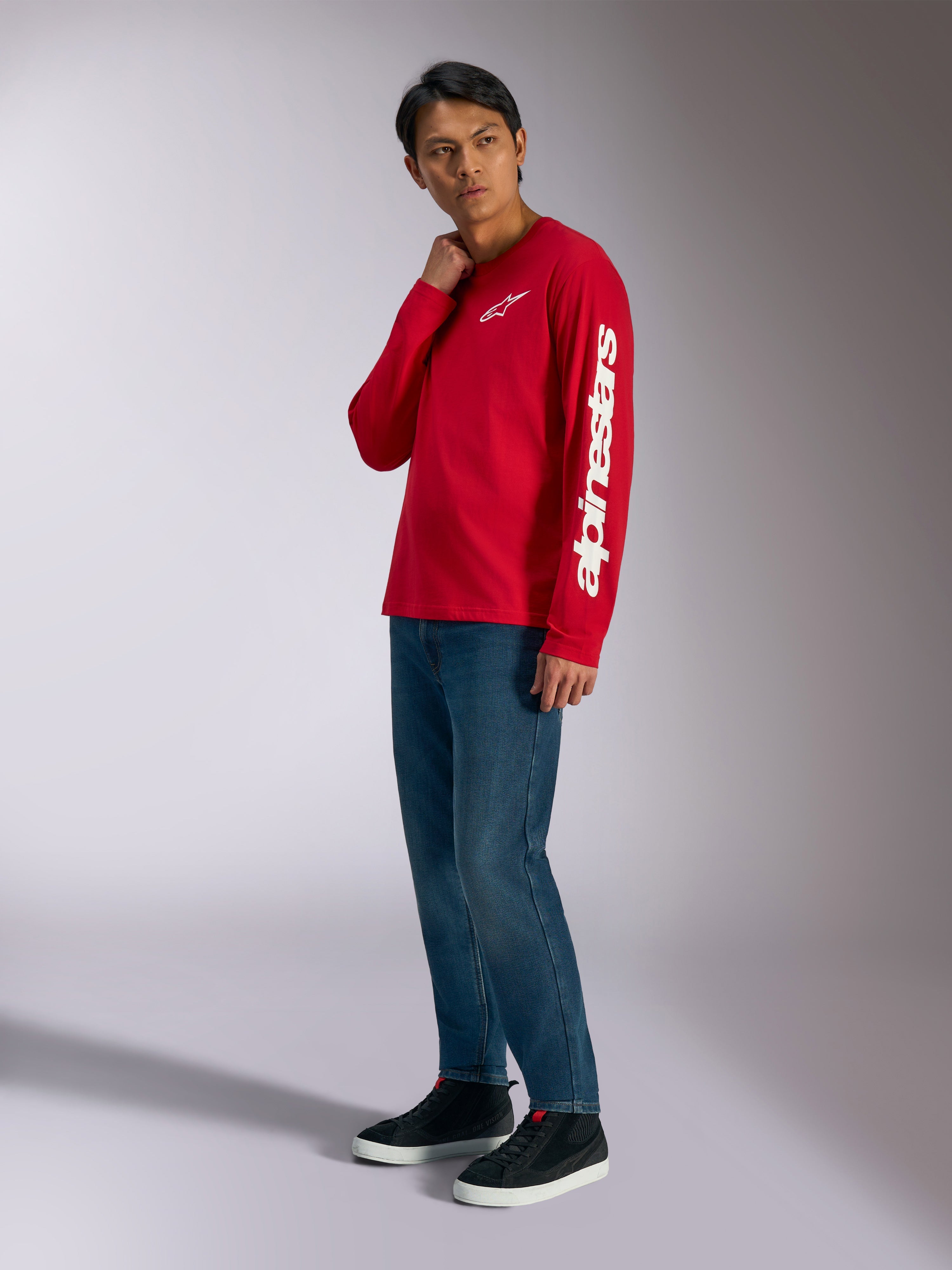 Alpinestars Trackside CSF Long Sleeve Tee, Red with white Alpinestars branding on chest and sleeve, worn by model with blue jeans and black sneakers, casual motorsport-inspired streetwear