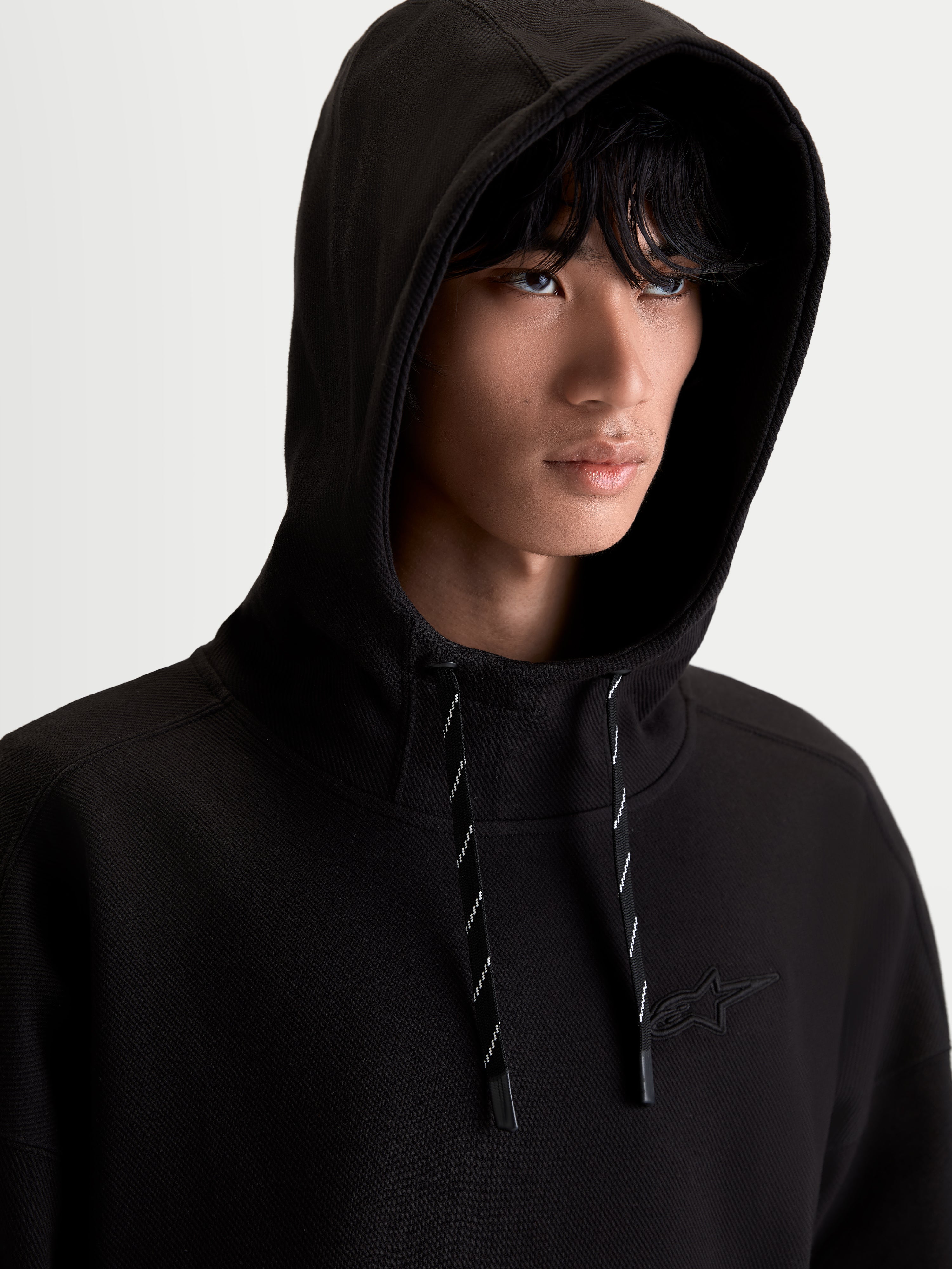 Alpinestars Camino Textured Oversized Hoodie, Black Men's Sportswear Pullover, featuring a high collar, textured knit twill fleece construction, and tonal embroidered logo, shown on model for a relaxed lifestyle look.