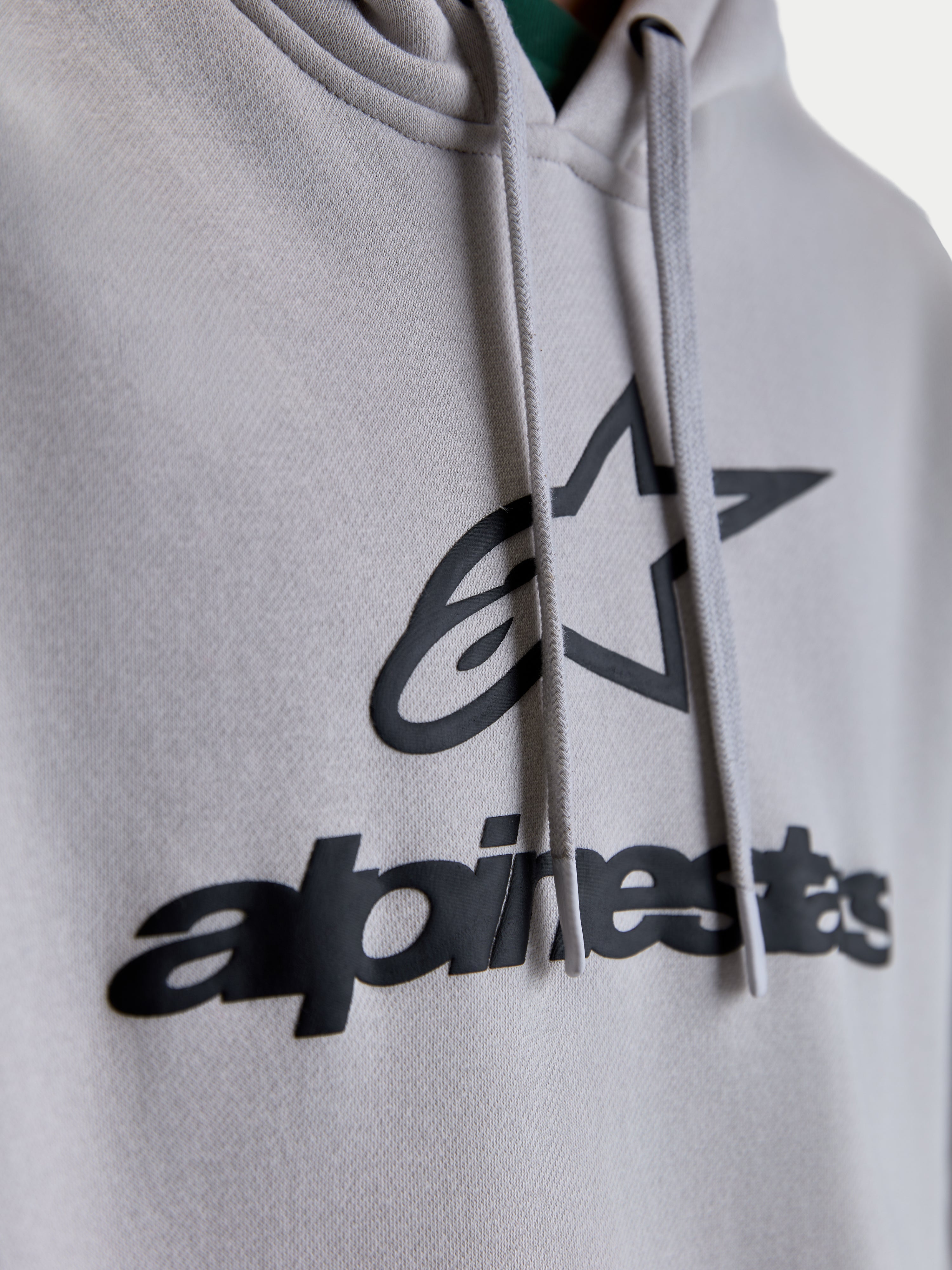 Alpinestars Prelude Oversized Hoodie, Sportswear Fleece Pullover, Unisex, Cement Gray and Black, Close-up of puff-print Alpinestars chest logo and flat hood drawcords.