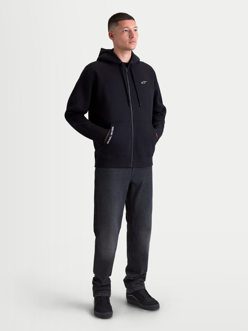 Alpinestars Pioneer Oversized Hoodie, Sportswear Full-Zip Fleece for Men and Women, Black, Cotton-Rich Blend, featuring a Vislon zipper, kangaroo pocket with 'ONE GOAL. ONE VISION.' branding, and white Astars chest logo. On-model view showing the relaxed oversized fit designed for casual everyday wear.