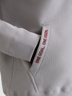 Alpinestars Pioneer Oversized Hoodie, Casual Sportswear Fleece in Cement Gray, Close-up of Kangaroo Pocket with Red 'ONE GOAL. ONE VISION.' Embroidery and Ribbed Cuffs