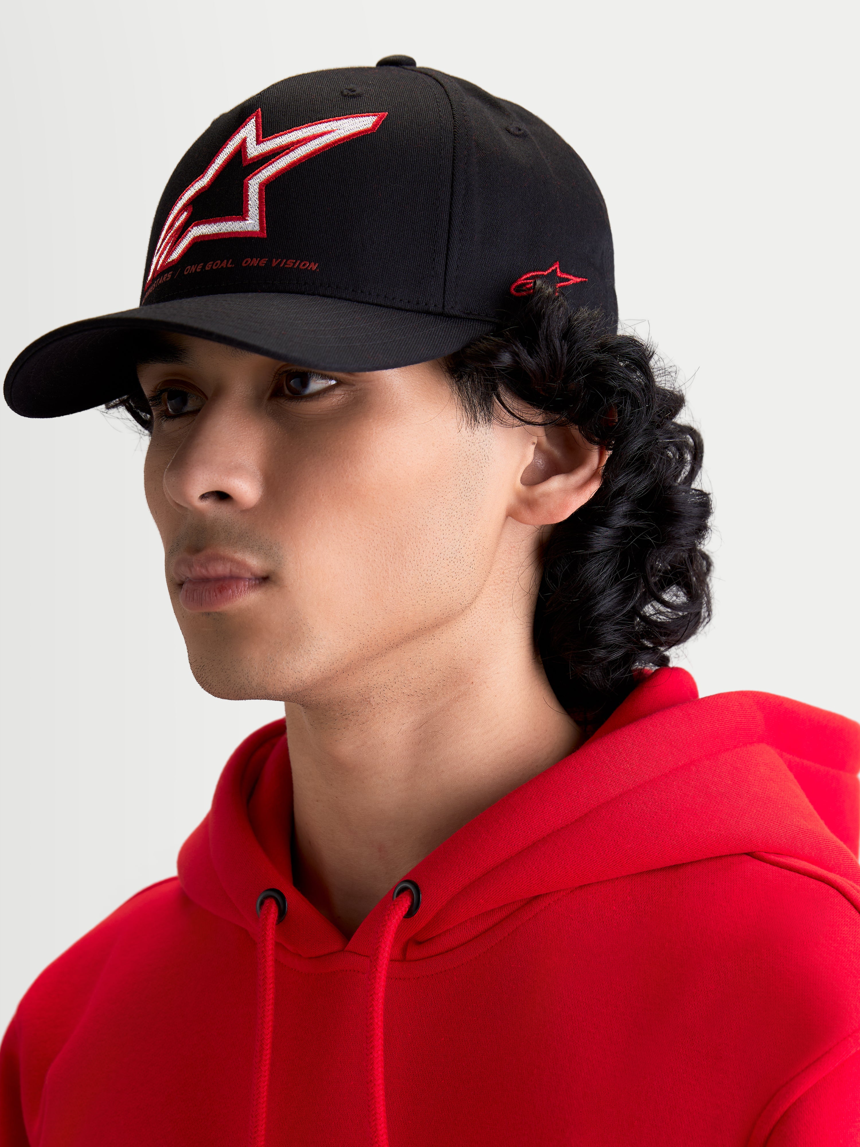 Alpinestars Lineout Hat, Black Curved Bill Sportswear Baseball Cap, featuring a structured crown with red and white embroidered Astars logo and side branding, shown on a model.