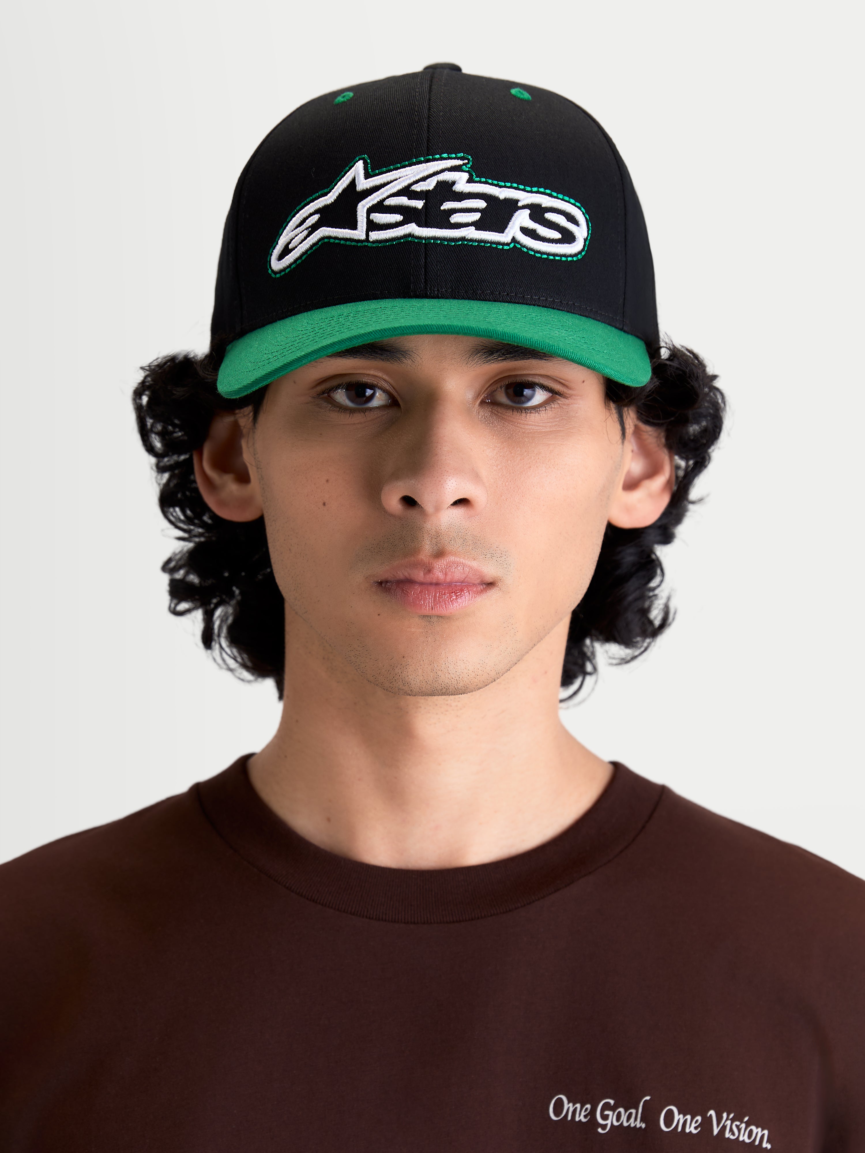 Alpinestars Retro Snapback Hat, Sportswear Lifestyle Cap, Black and Green, featuring a curved bill, structured crown, and front embroidered Astars logo with green running stitch, shown on model front view.