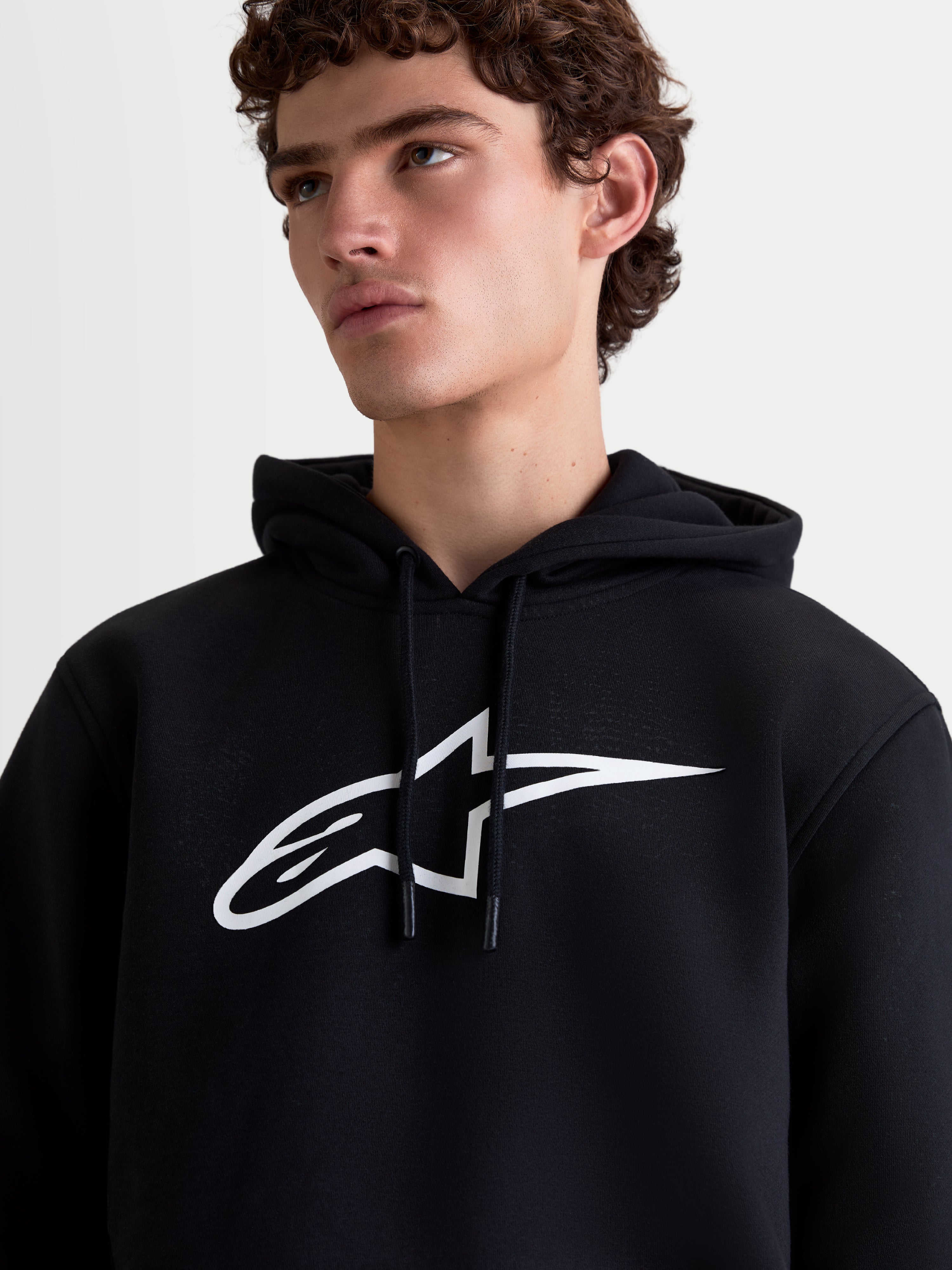 Alpinestars Ageless V3 Hoodie, Men's Sportswear Pullover Fleece, Black and White, close-up on-model view featuring a large white chest logo and drawstring hood.