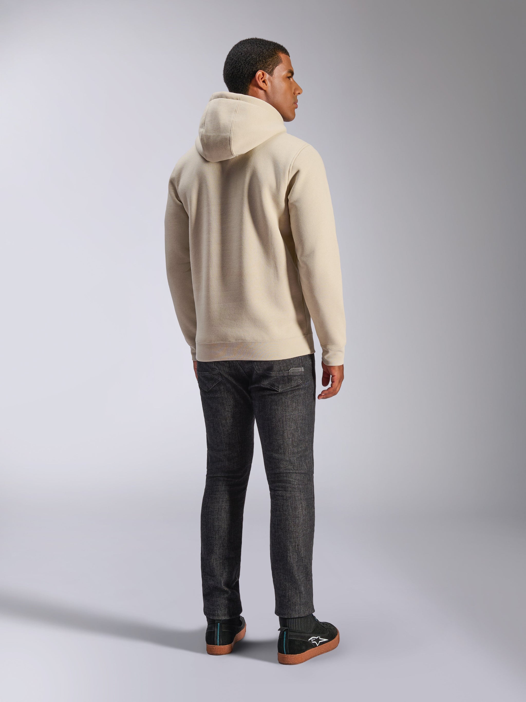 Alpinestars Ageless V3 Hoodie, casual off-white hooded pullover fleece shown from the back, features ribbed cuffs and hem, worn with dark slim-fit jeans and black Alpinestars sneakers