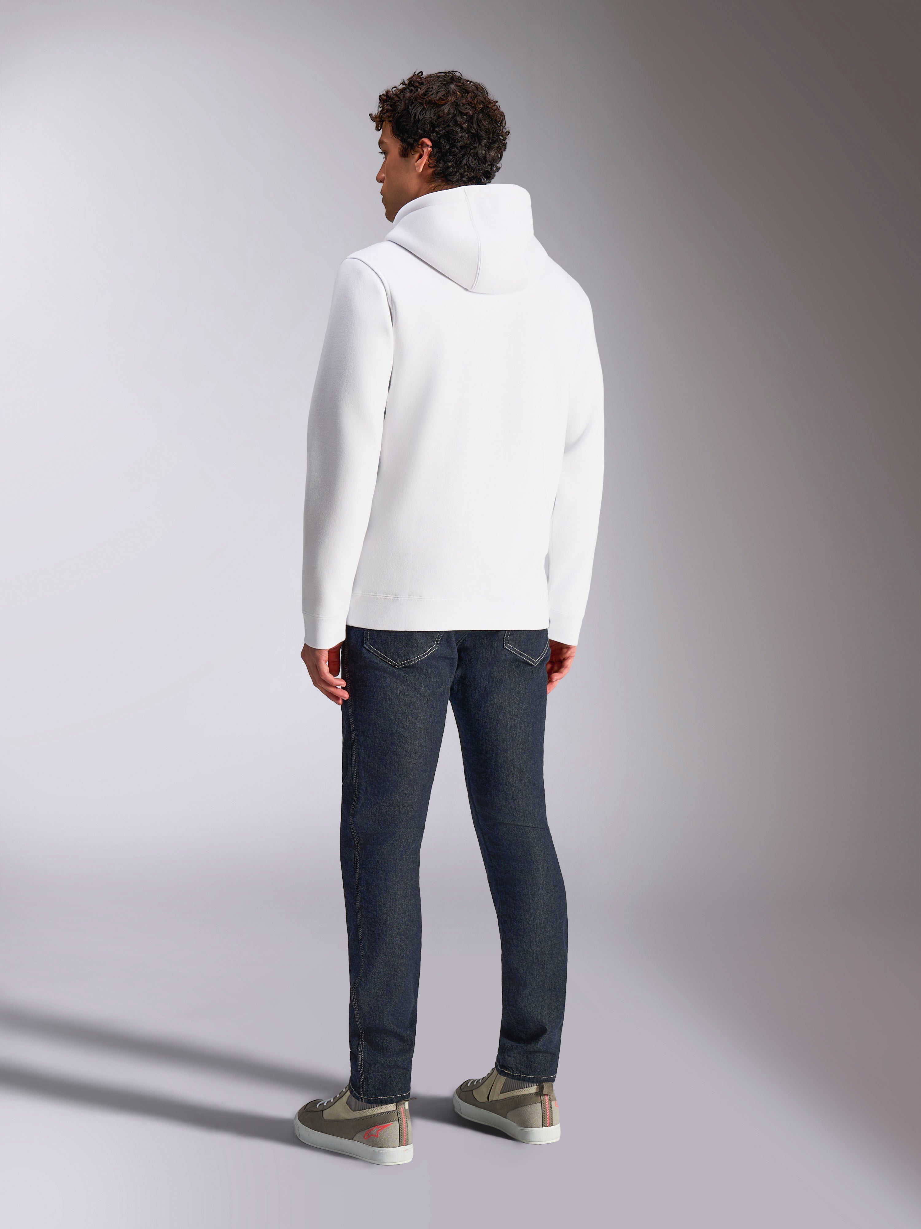 Alpinestars Blaze V3 Hoodie, back view of male model wearing a white pullover hoodie, casual sportswear styled with dark blue jeans and grey sneakers, modern motorsport-inspired design