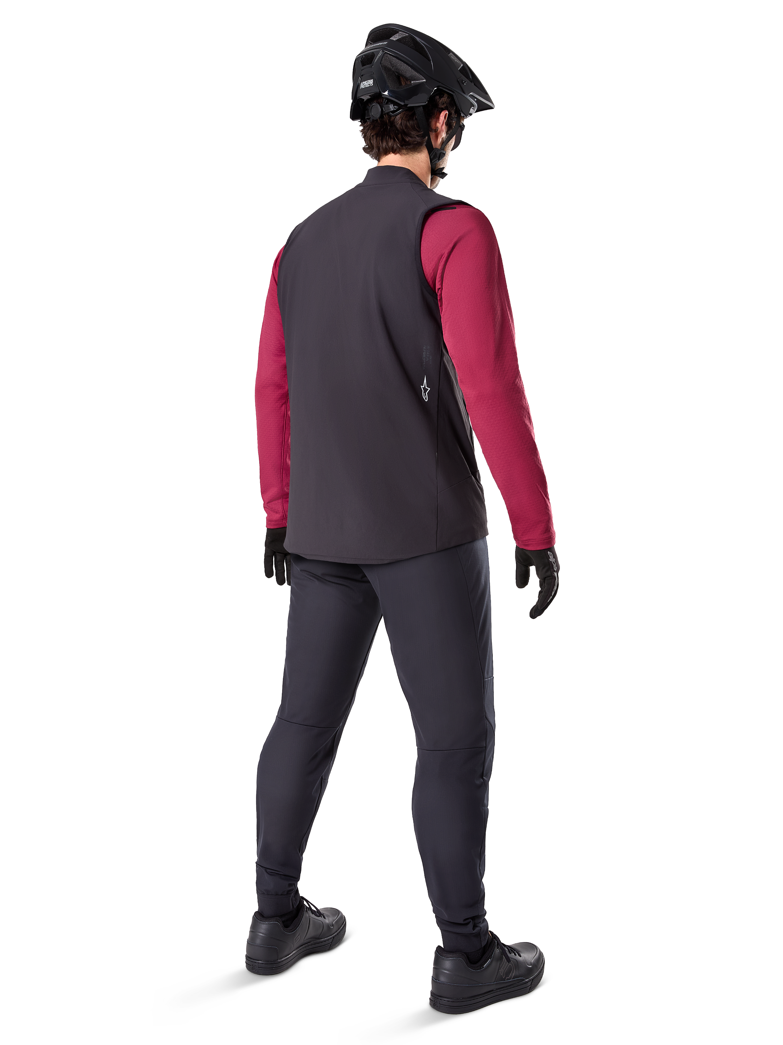Alpinestars A-Dura Thermal Vest, Black cycling vest, shown from the back on a model wearing a maroon long-sleeve jersey and black cycling pants, paired with a black mountain bike helmet and gloves, technical gear for cold-weather riding
