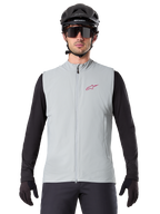 Alpinestars A-Dura Thermal Vest, Cycling Gilet, Titanium Gray, worn with a black long-sleeve jersey and black cycling helmet, red Alpinestars star logo on chest, lightweight and insulated for mountain biking.