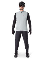 Alpinestars A-Dura Thermal Vest, cycling vest, Titanium Gray, worn with black long-sleeved jersey and black trousers, black helmet and sunglasses, featuring a red Alpinestars logo, lightweight thermal insulation for mountain biking