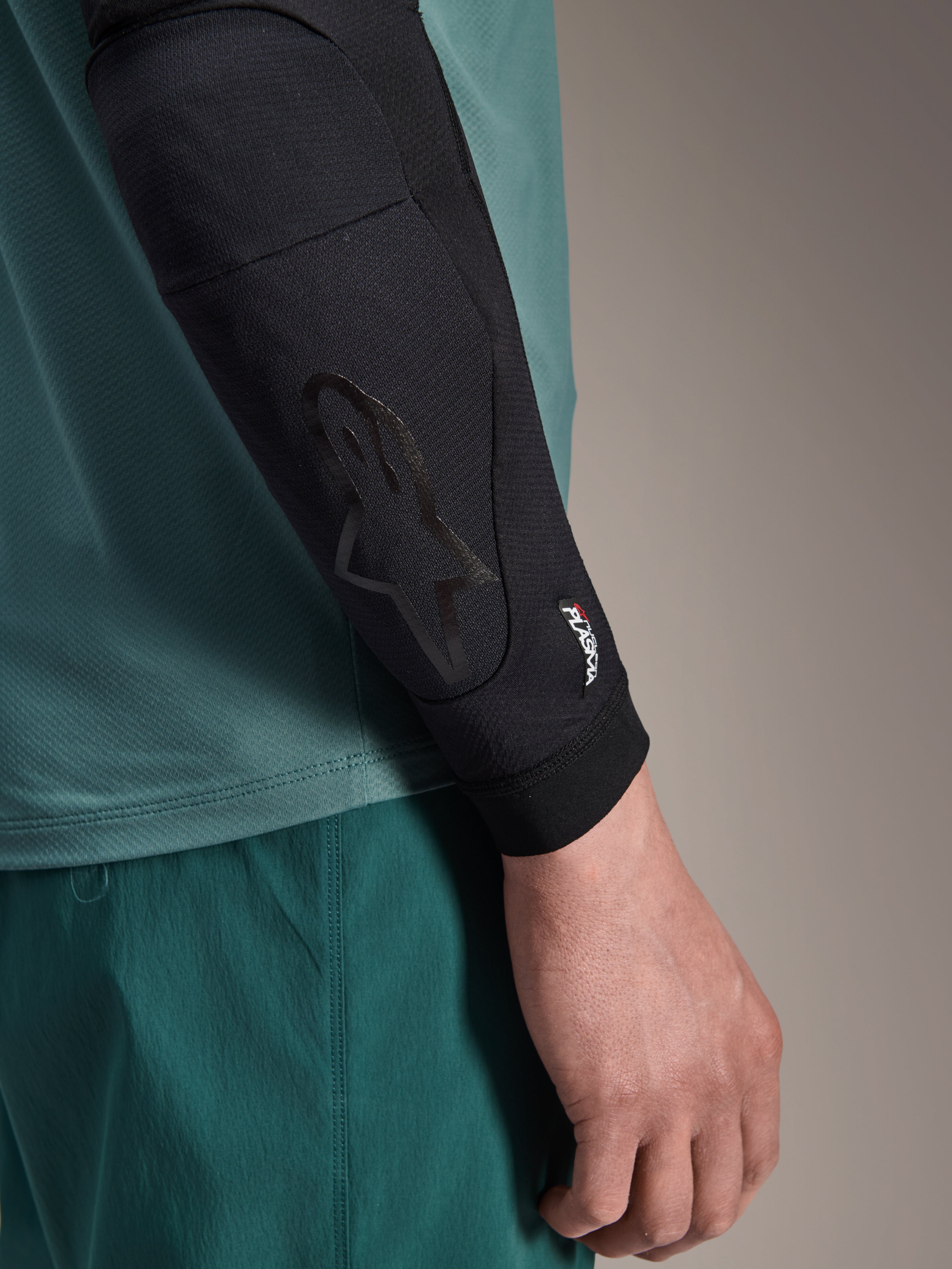 Alpinestars A-Motion Plasma Elbow Sleeve, Black, MTB Elbow Protector, close-up view worn on arm with teal jersey, featuring tonal Astars logo and Nucleon Plasma branding, slim-profile mesh design for off-road cycling