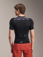 Alpinestars A-Motion Plasma Protection Jacket - Short Sleeve, Black with Grey Camo accents on the upper back, back view showing integrated back protector and white Astars logo at the hem, worn with red shorts, technical mountain bike protection gear