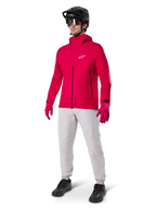 Model wearing Alpinestars A-Dura Waterproof Pants in Titanium gray, paired with a bright red waterproof jacket and matching gloves, black mountain bike helmet with goggles, and black shoes, full mountain biking gear for wet trail conditions