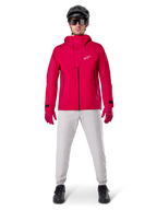 Alpinestars A-Dura Waterproof Pants, MTB Pants, Titanium Gray, worn with a bright red hooded jacket, red gloves, and a black mountain bike helmet, professional waterproof cycling gear for wet trail conditions