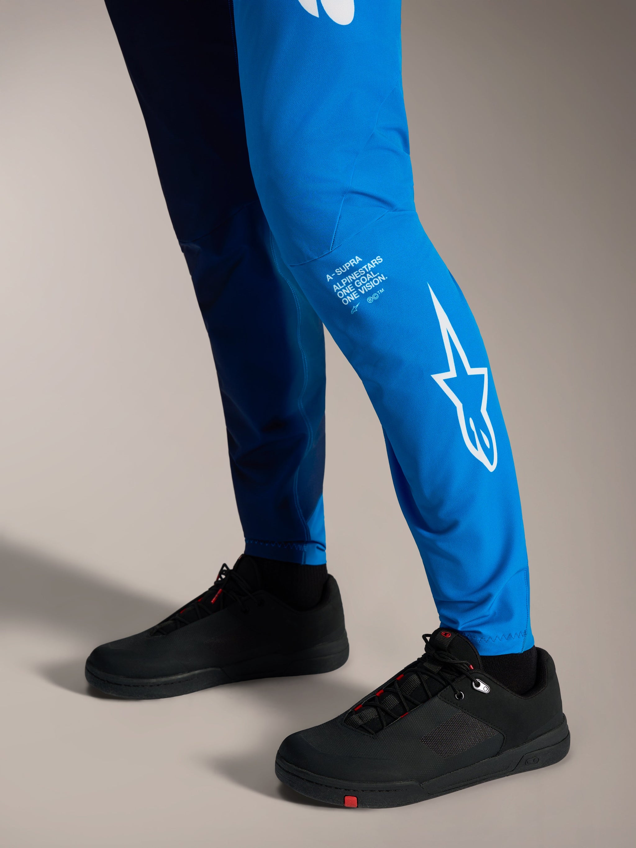 Faded Bright Blue A-Supra Elite Pants featuring white Astars branding on the lower leg and black MTB shoes.