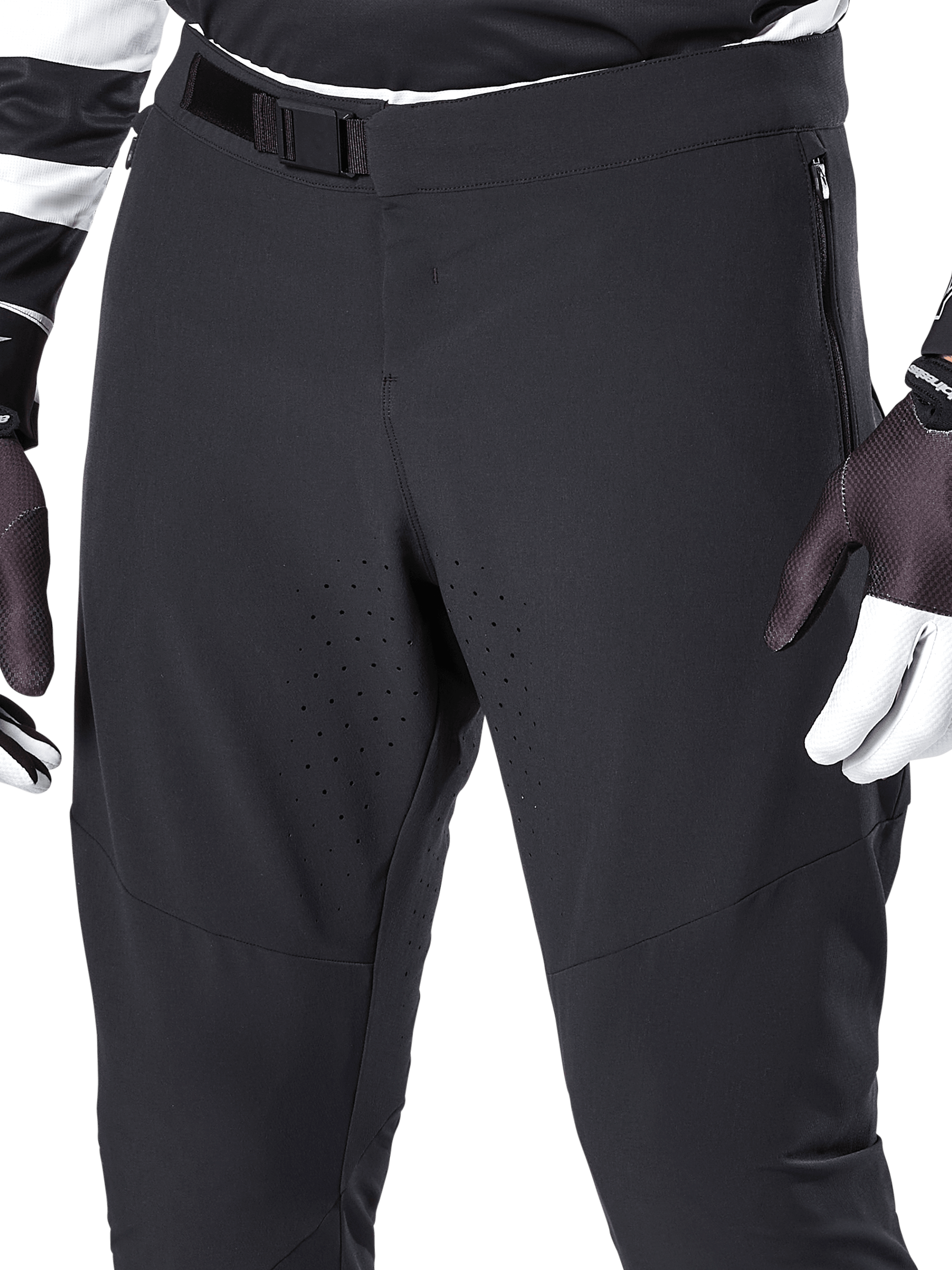 Alpinestars A-Aria Elite Pants, Black mountain bike pants, close-up of front waist and thighs featuring magnetic buckle closure and laser-cut ventilation holes, paired with cycling gloves