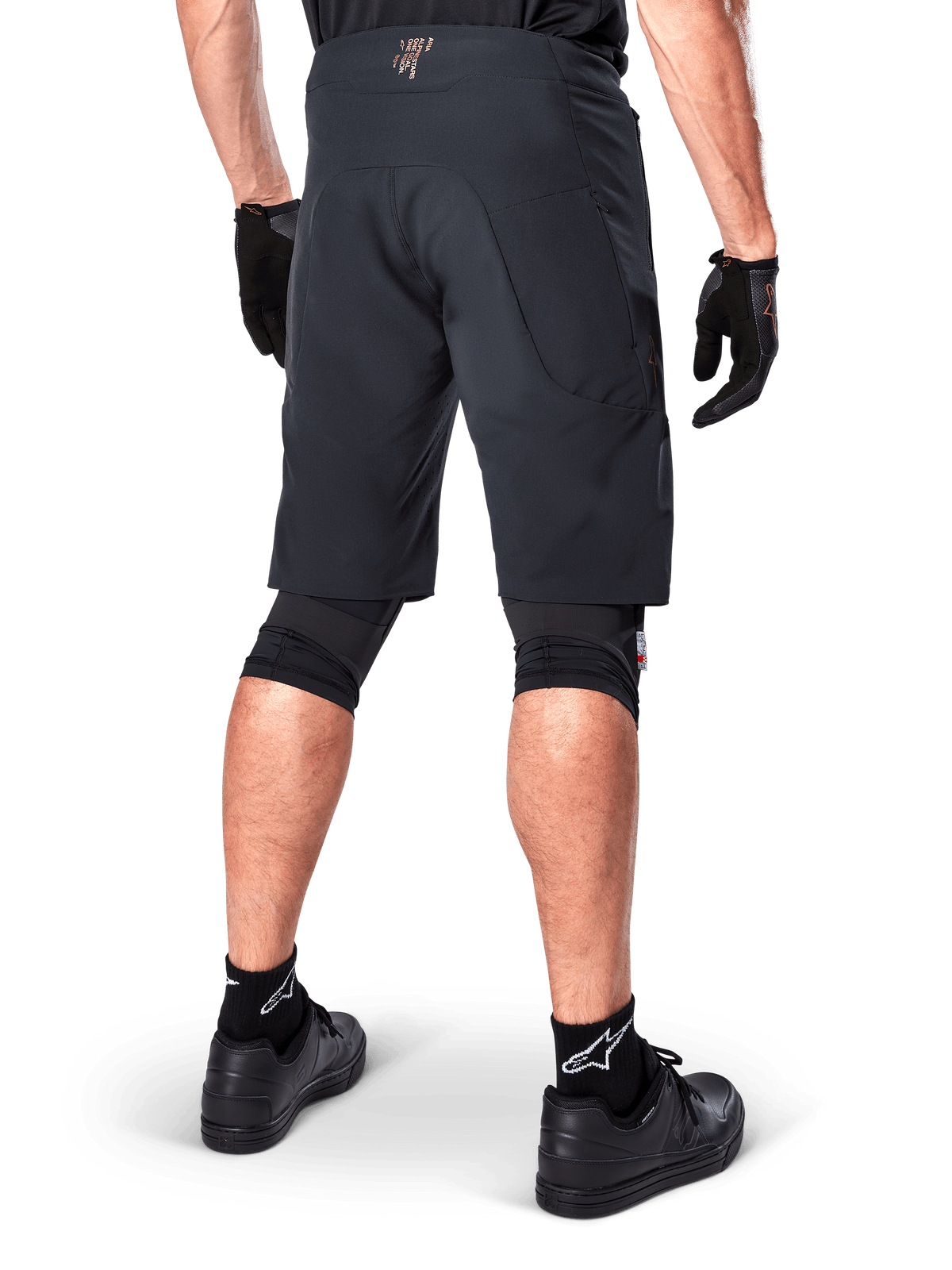 Rear view of a rider wearing Alpinestars A-Aria Elite Shorts in Black, performance mountain bike shorts, styled with black cycling gloves and black shoes, designed for flexible movement on off-road trails