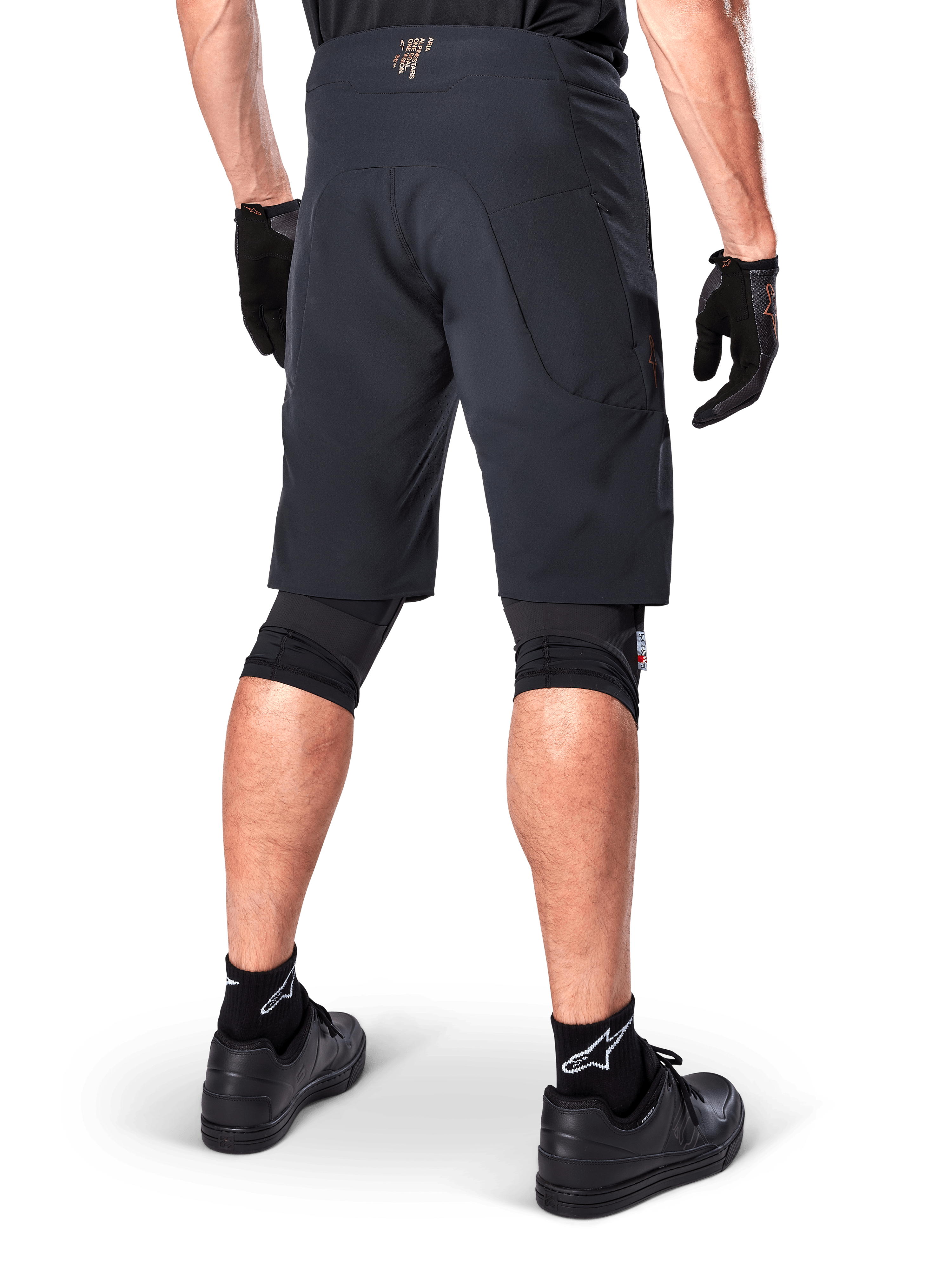 Rear view of a rider wearing Alpinestars A-Aria Elite Shorts in Black, performance mountain bike shorts, styled with black cycling gloves and black shoes, designed for flexible movement on off-road trails