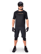 Male mountain bike rider wearing Alpinestars A-Aria Elite Shorts in Black, paired with a matching black Alpinestars short-sleeve jersey, black helmet, gloves, and knee guards, complete off-road cycling gear outfit