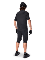 Rear view of a mountain biker wearing Alpinestars A-Aria Elite Shorts in Black, paired with a matching black short-sleeve jersey, black helmet, gloves, and MTB shoes, showing a complete performance outfit for off-road cycling.