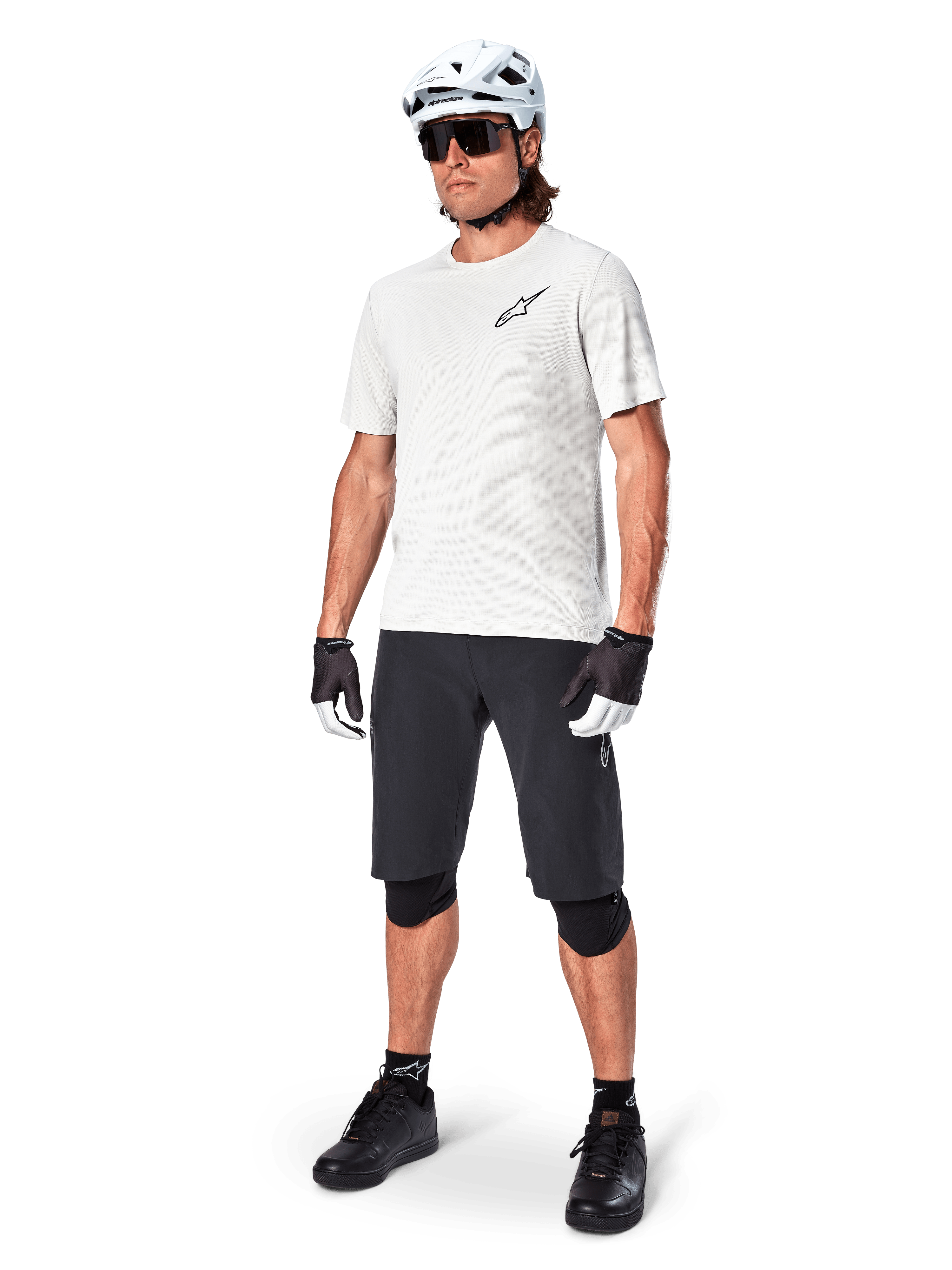 Male mountain biker wearing Alpinestars A-Aria Shorts, Black cycling shorts, styled with a white short-sleeve jersey, white mountain bike helmet, and black performance gear, full outfit for off-road trail riding