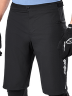 Alpinestars A-Dura Elite Shorts, Black MTB Shorts, close-up view featuring front snap closure and zippered side pocket, worn by a rider with black cycling gloves and knee pads, performance gear for mountain biking
